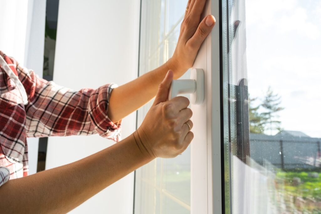 The hand holds the handle of a plastic double glazed window, clo